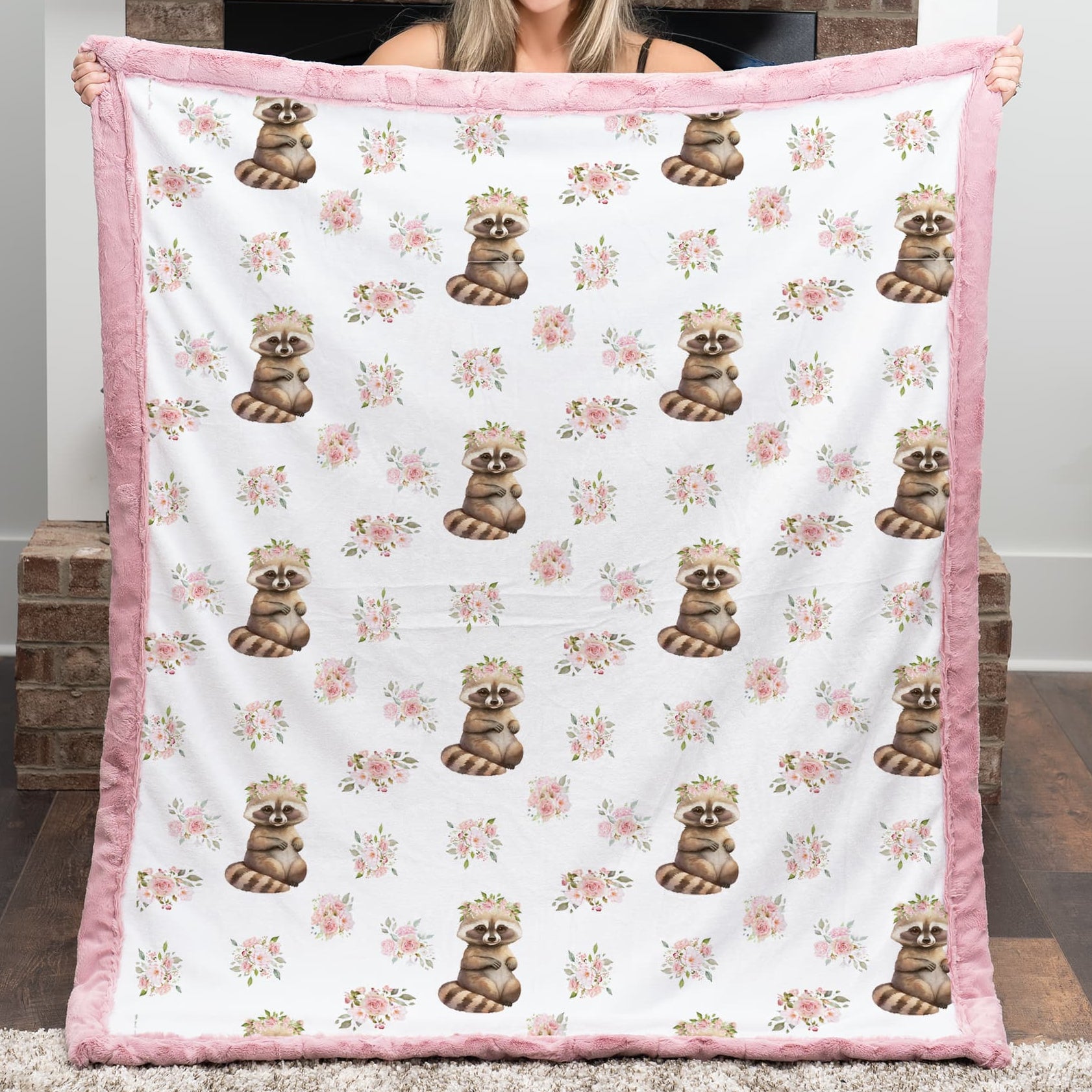 Woman holding a floral-patterned blanket with raccoon designs in a room.