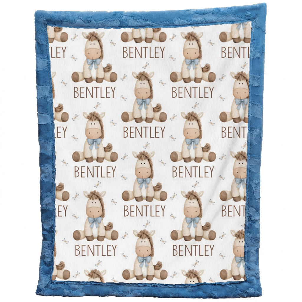 A personalized baby blanket featuring a repeating pattern of brown cartoon horses wearing blue bows, with the name 'BENTLEY' printed below each horse. The blanket has a solid blue ruffled border and is shown flat against a white background.