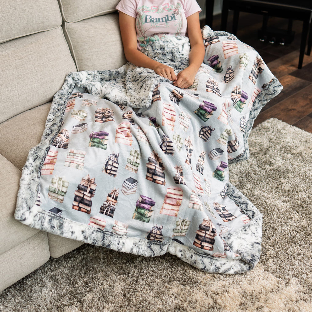 Person sitting on a couch with a blanket featuring book patterns