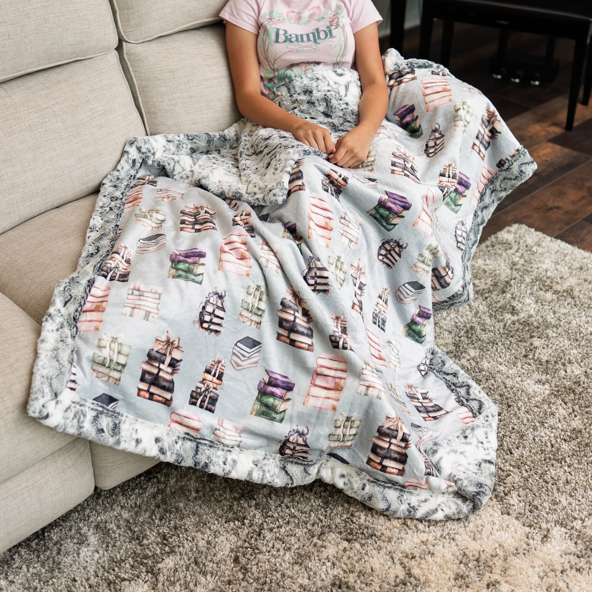 Person sitting on a couch with a blanket featuring book patterns