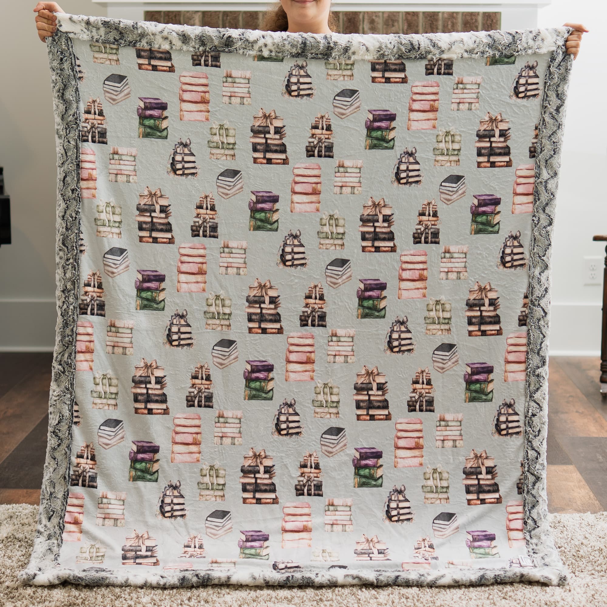 Person holding a blanket with book pattern in a room.