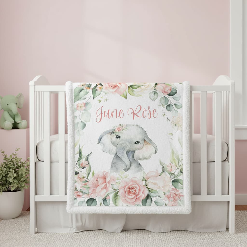 Baby crib with a floral elephant blanket featuring the name 'Julie Rose' on a pink wall.