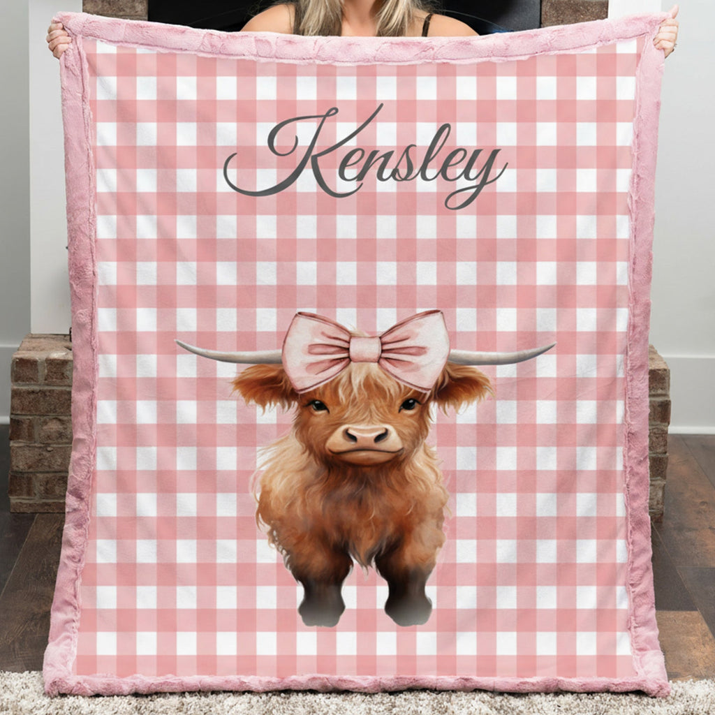 Person holding a pink checkered blanket with a cow illustration and 'Kensley' text.