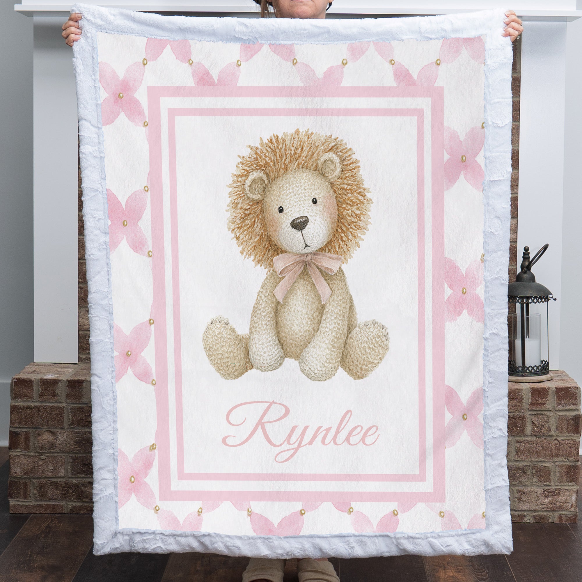 Personalized lion baby blanket with white fur trim, pink floral border, held by fireplace mantel