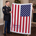 Personalized American flag blanket with family name held by soldier and woman near Christmas tree