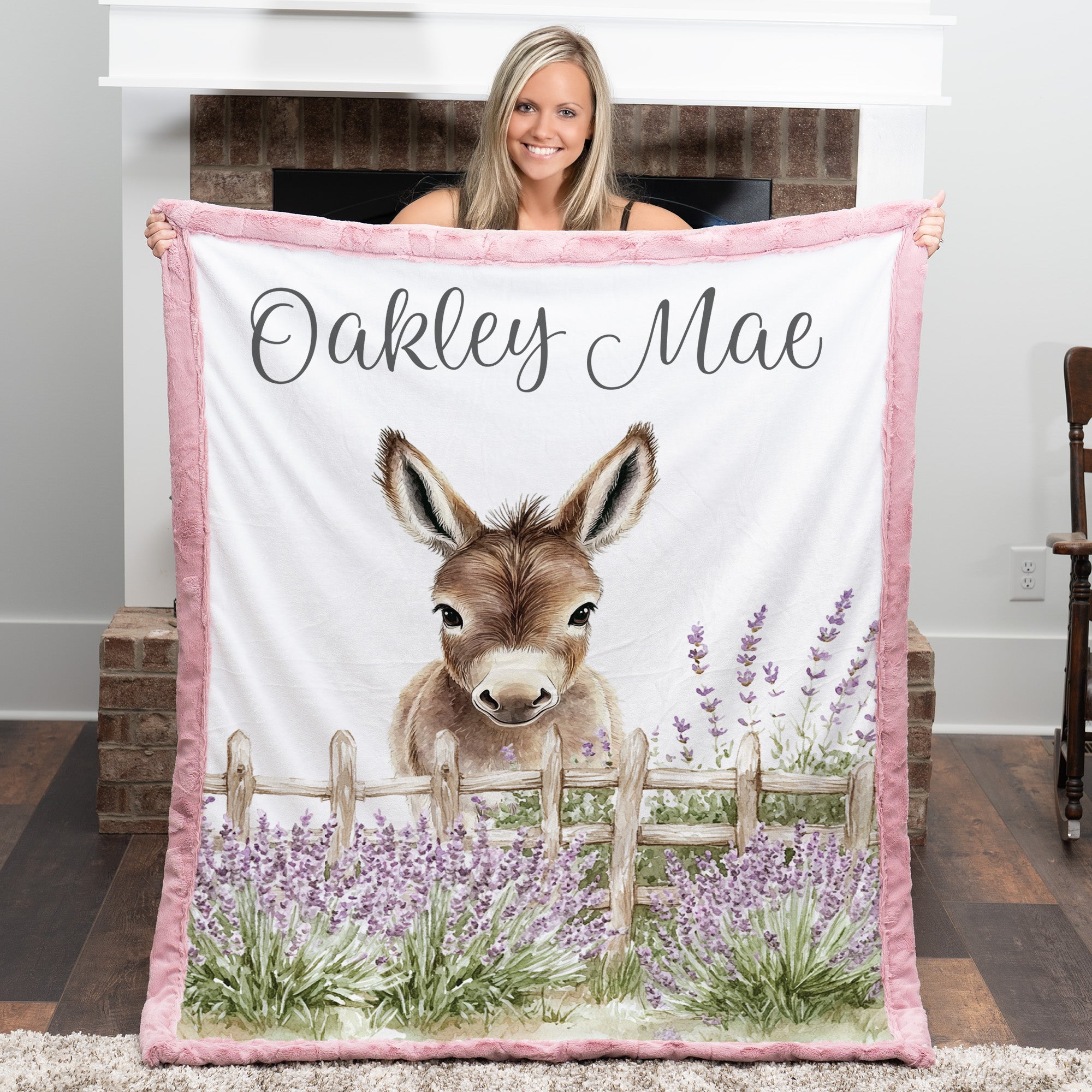 Woman holding personalized baby donkey minky blanket with pink trim over fireplace mantel