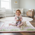 Toddler girl sitting on personalized baby donkey minky blanket with plush toys in nursery