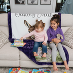 Two girls sitting on personalized baby donkey minky blanket with purple trim on couch