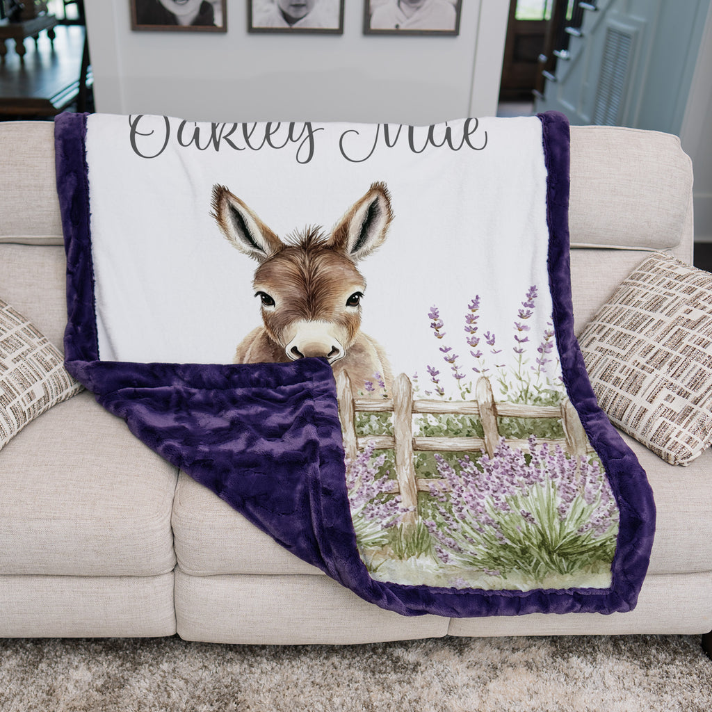 Personalized baby donkey minky blanket with purple trim draped over couch in living room