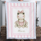Personalized minky ballerina frog baby blanket with pink stripe border held up by fireplace