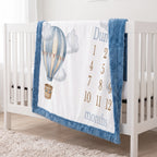 Personalized hot air balloon milestone minky blanket with blue trim hanging on crib rail