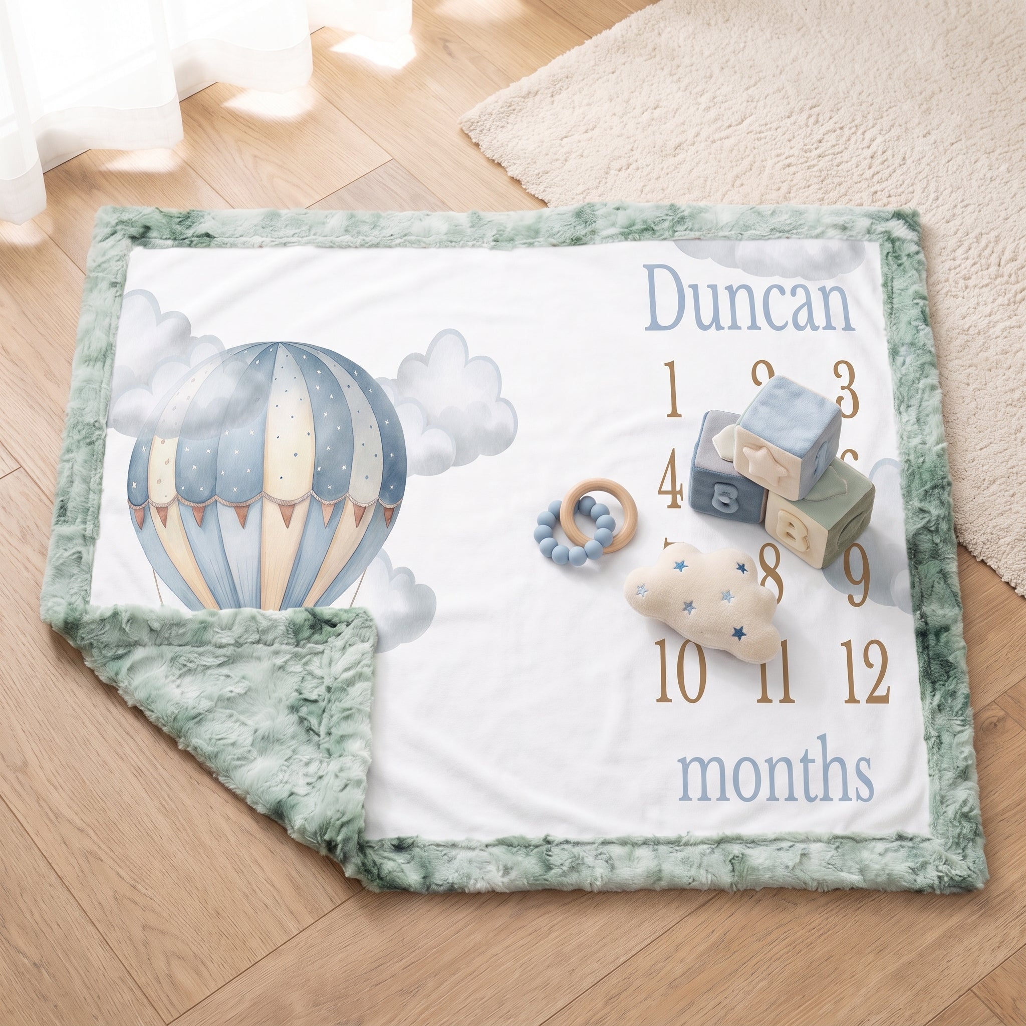 Personalized hot air balloon milestone minky blanket with sage trim flat-laid with baby toys