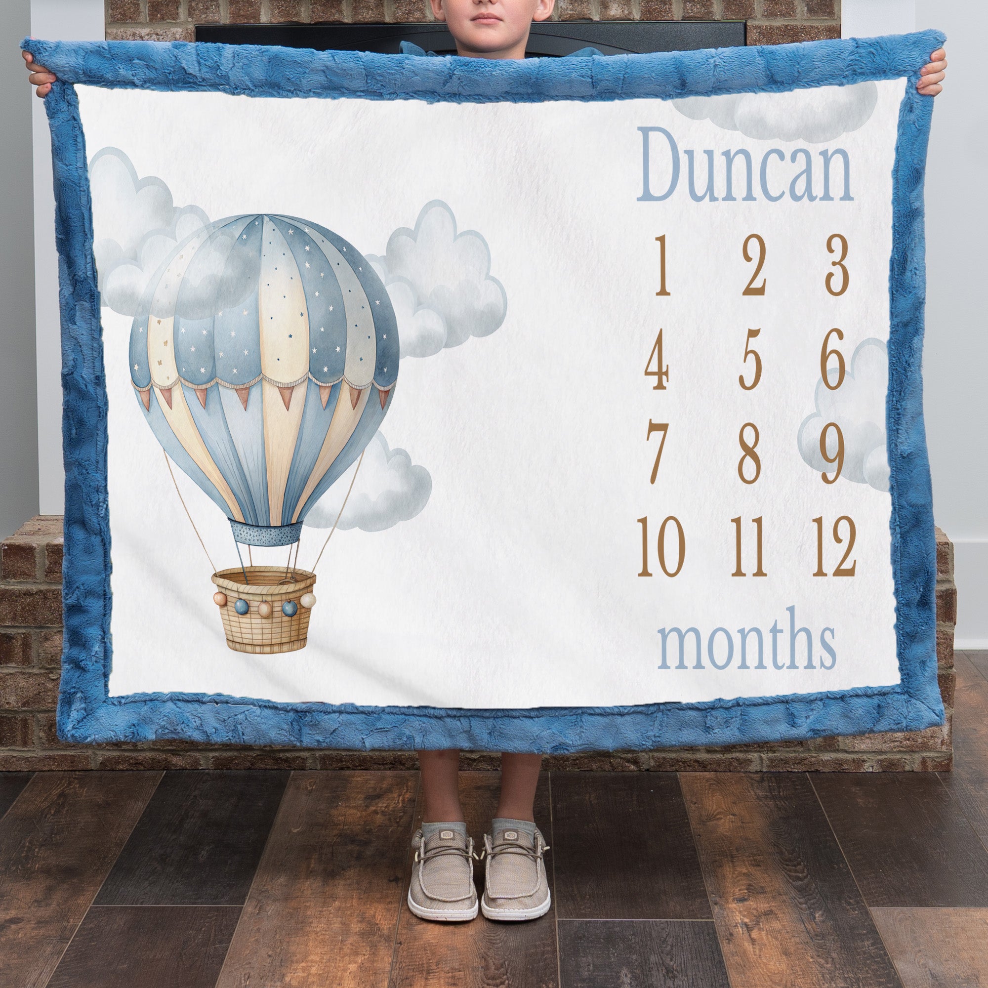 Personalized hot air balloon milestone minky blanket with blue trim held up by child