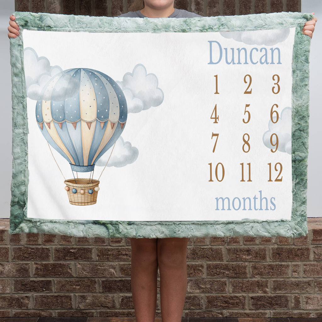 Personalized hot air balloon milestone minky blanket with sage trim held up outdoors