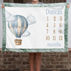 Personalized hot air balloon milestone minky blanket with sage trim held up outdoors