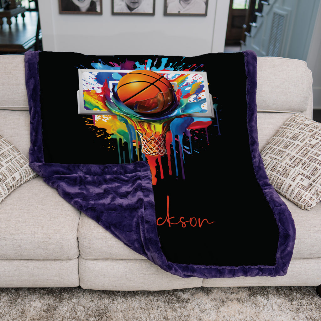 Basketball Luxe Cuddle blanket with purple border draped over sofa arm, colorful paint-splash hoop art