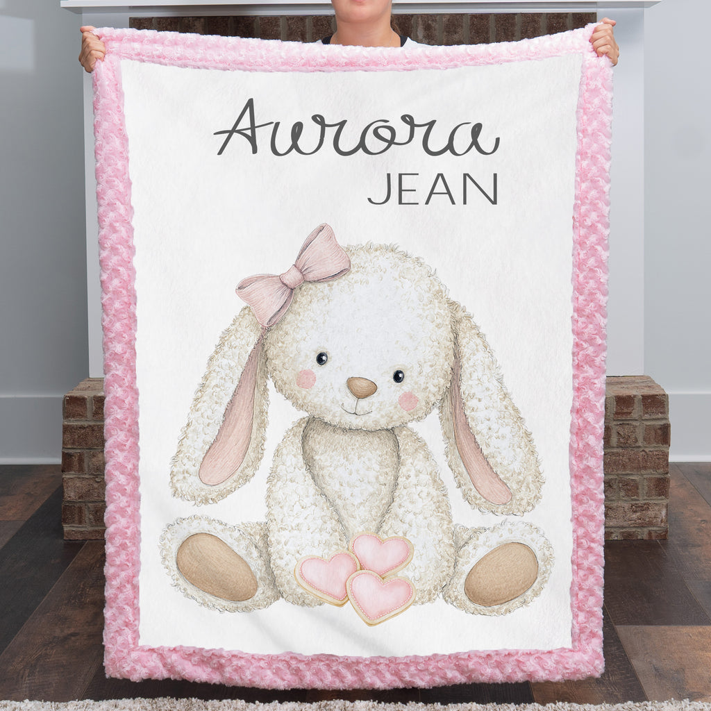 Woman holding personalized bunny minky baby blanket with pink rosette border by fireplace