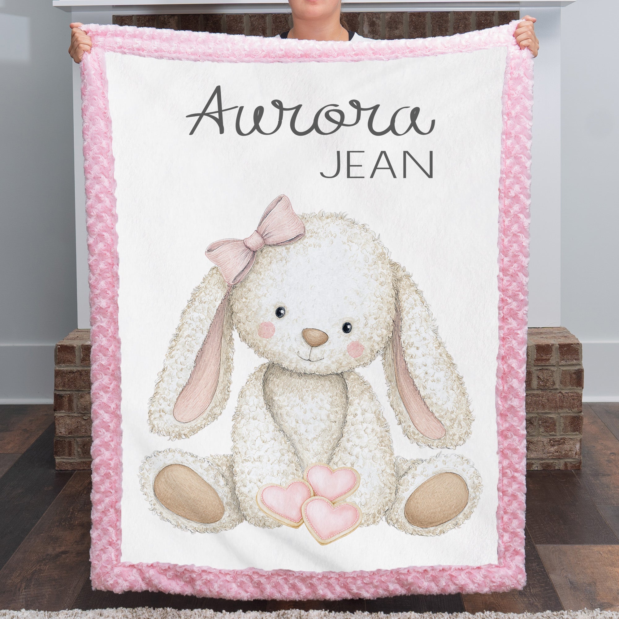 Woman holding personalized bunny minky baby blanket with pink rosette border by fireplace