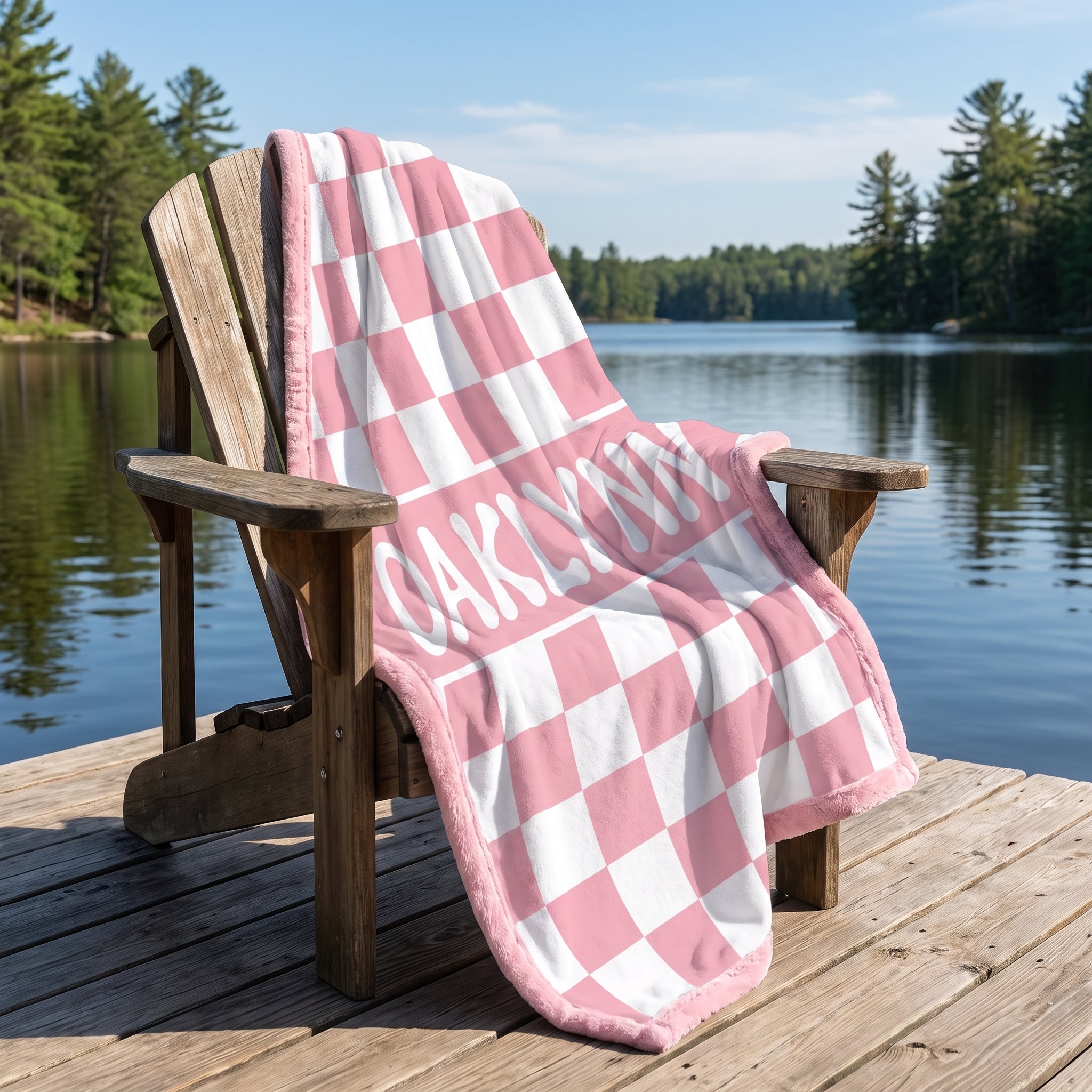 Personalized pink checkered minky baby blanket with Oaklynn's name draped over a lakeside chair