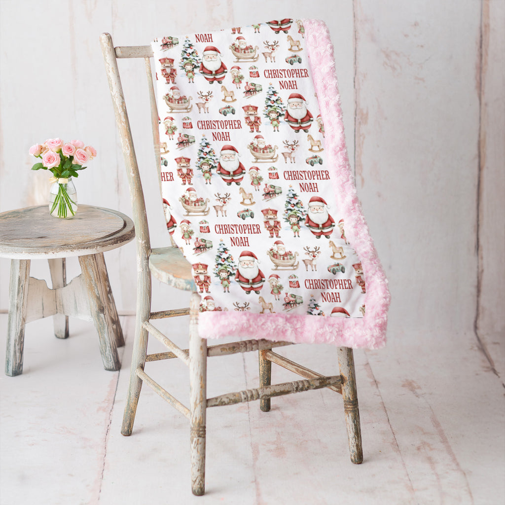 Personalized Christmas minky blanket with Santa print and pink trim draped on vintage chair