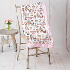Personalized Christmas minky blanket with Santa print and pink trim draped on vintage chair