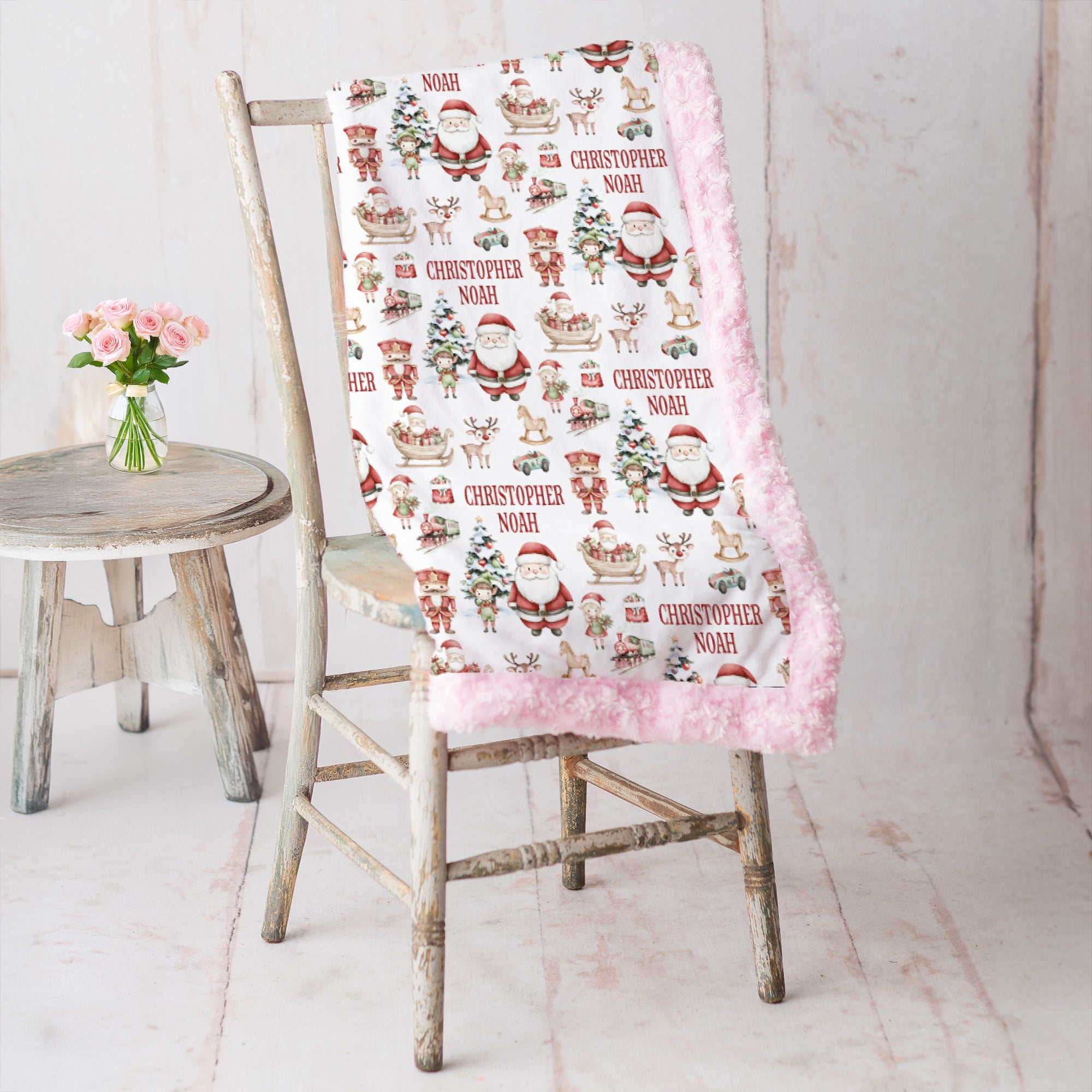 Personalized Christmas minky blanket with Santa print and pink trim draped on vintage chair