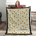 Black trim minky blanket with daisy floral print and personalized name, held by brick fireplace