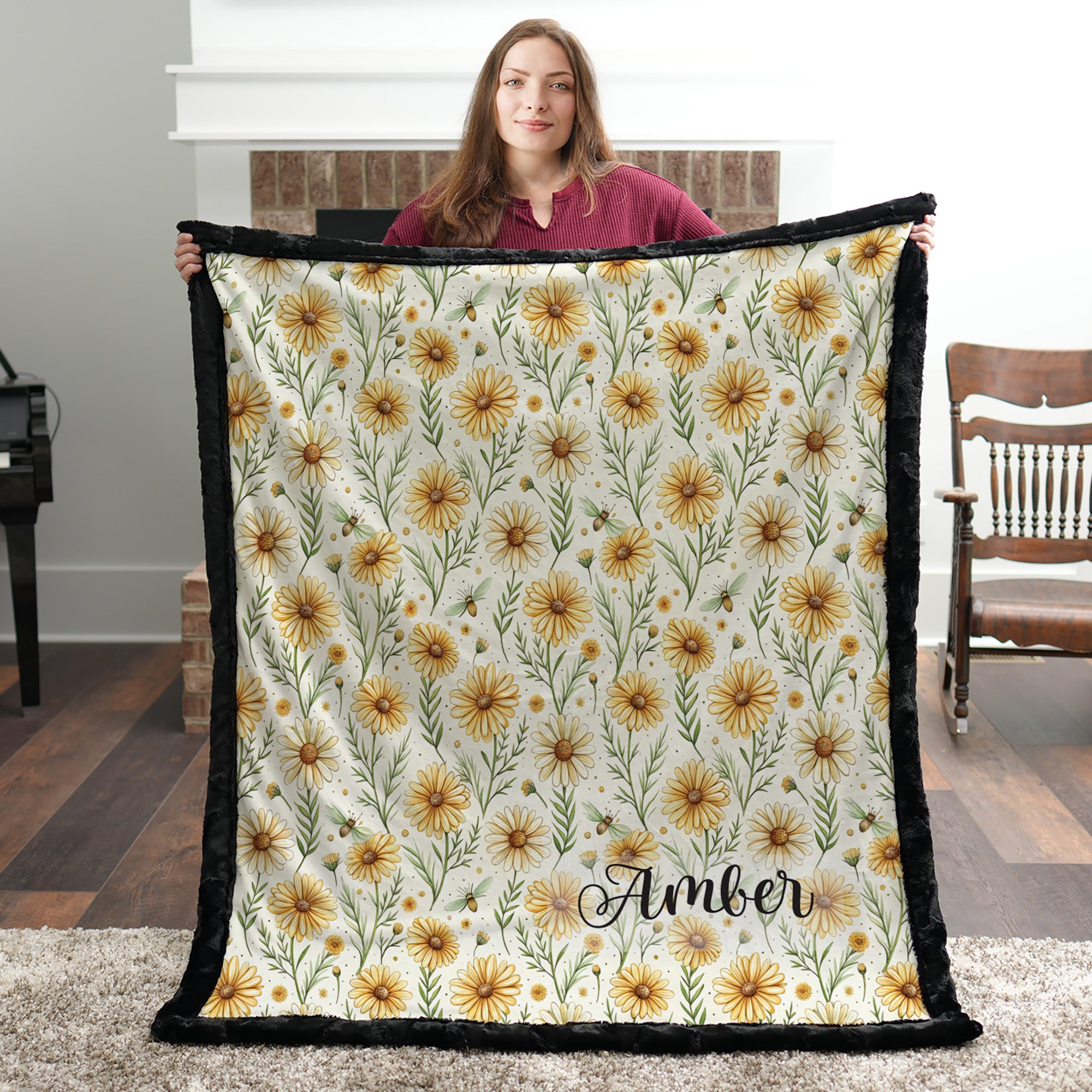 Black trim minky blanket with daisy floral print and personalized name, held by brick fireplace
