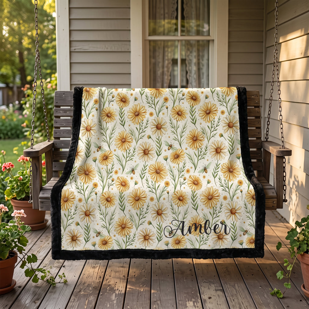Black trim minky blanket with daisy floral print and personalized name, draped over porch swing