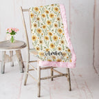 Pink trim minky blanket with daisy floral print and personalized name, draped over vintage chair
