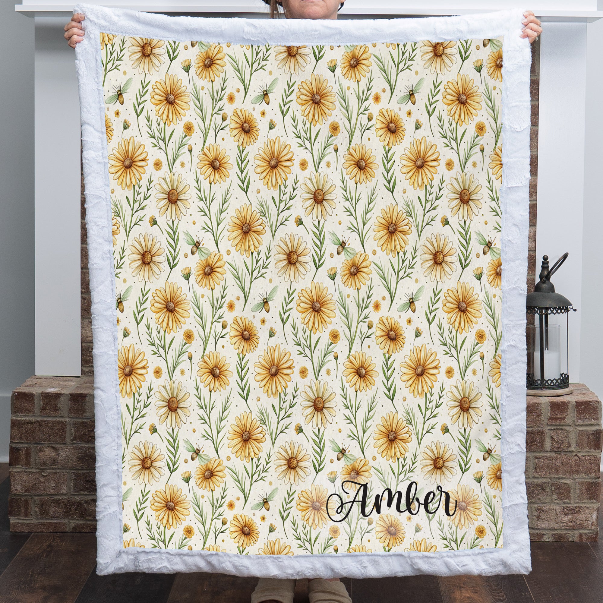 White trim minky blanket with daisy floral print and personalized name, held by brick fireplace