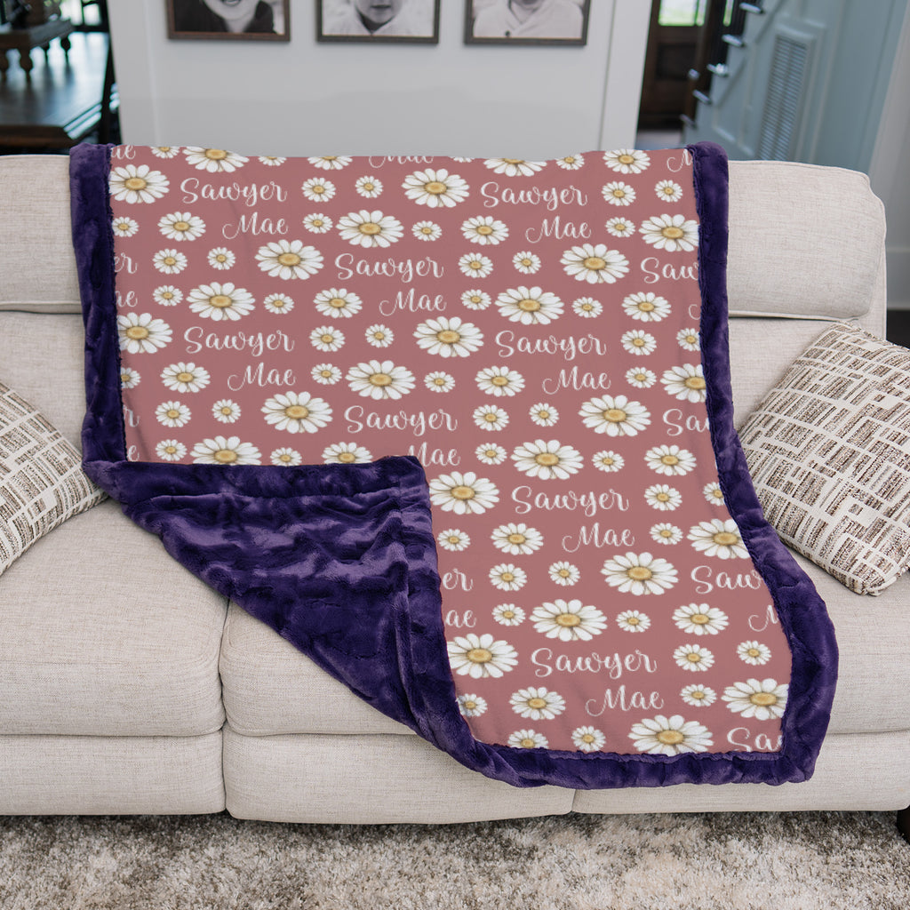 Two girls sitting on personalized daisy minky blanket with purple trim reading a book