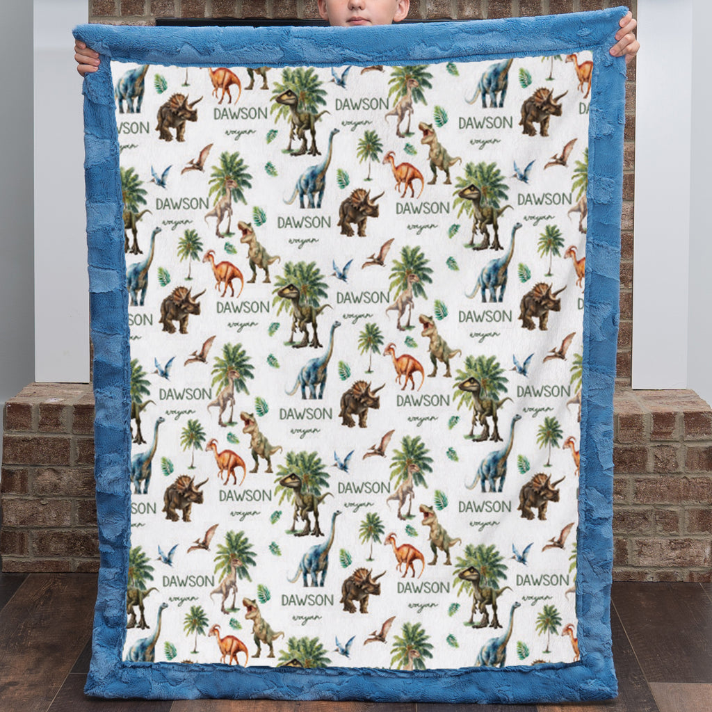 Personalized dinosaur minky baby blanket with custom name, held up by a boy, blue trim