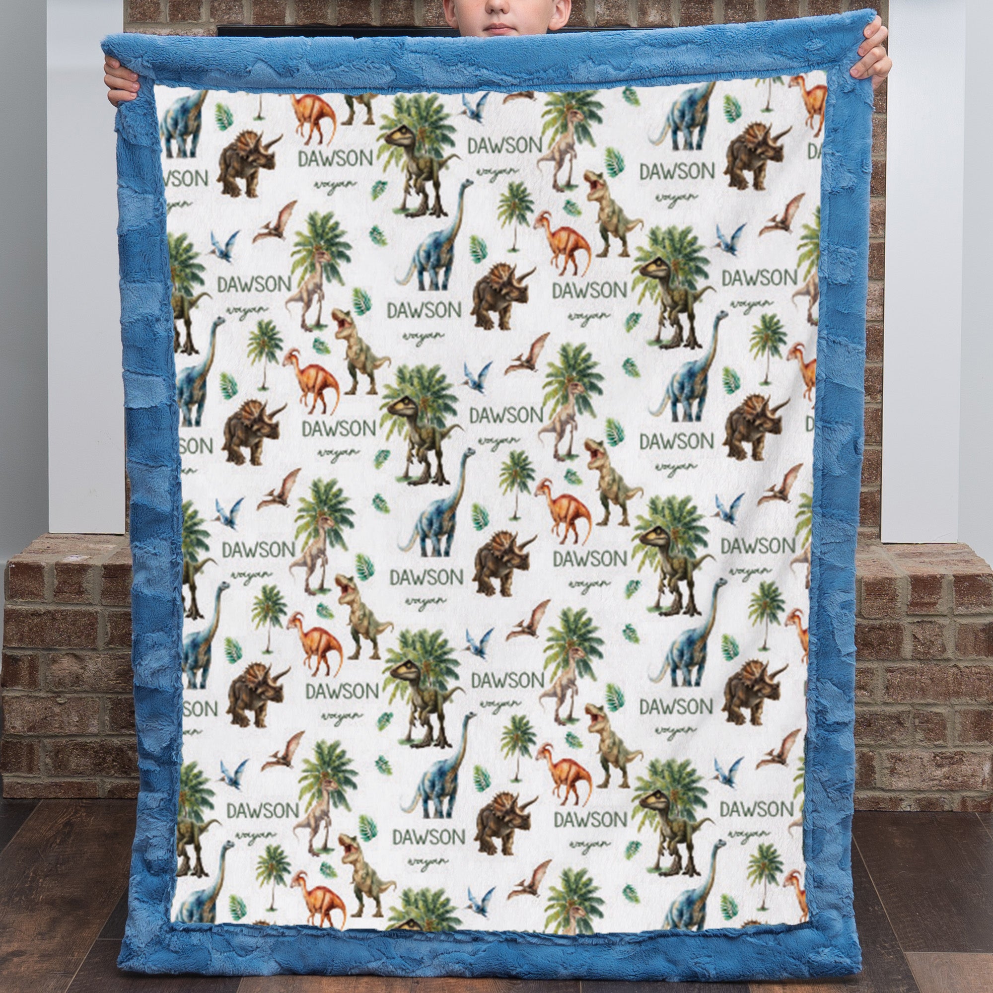 Personalized dinosaur minky baby blanket with custom name, held up by a boy, blue trim