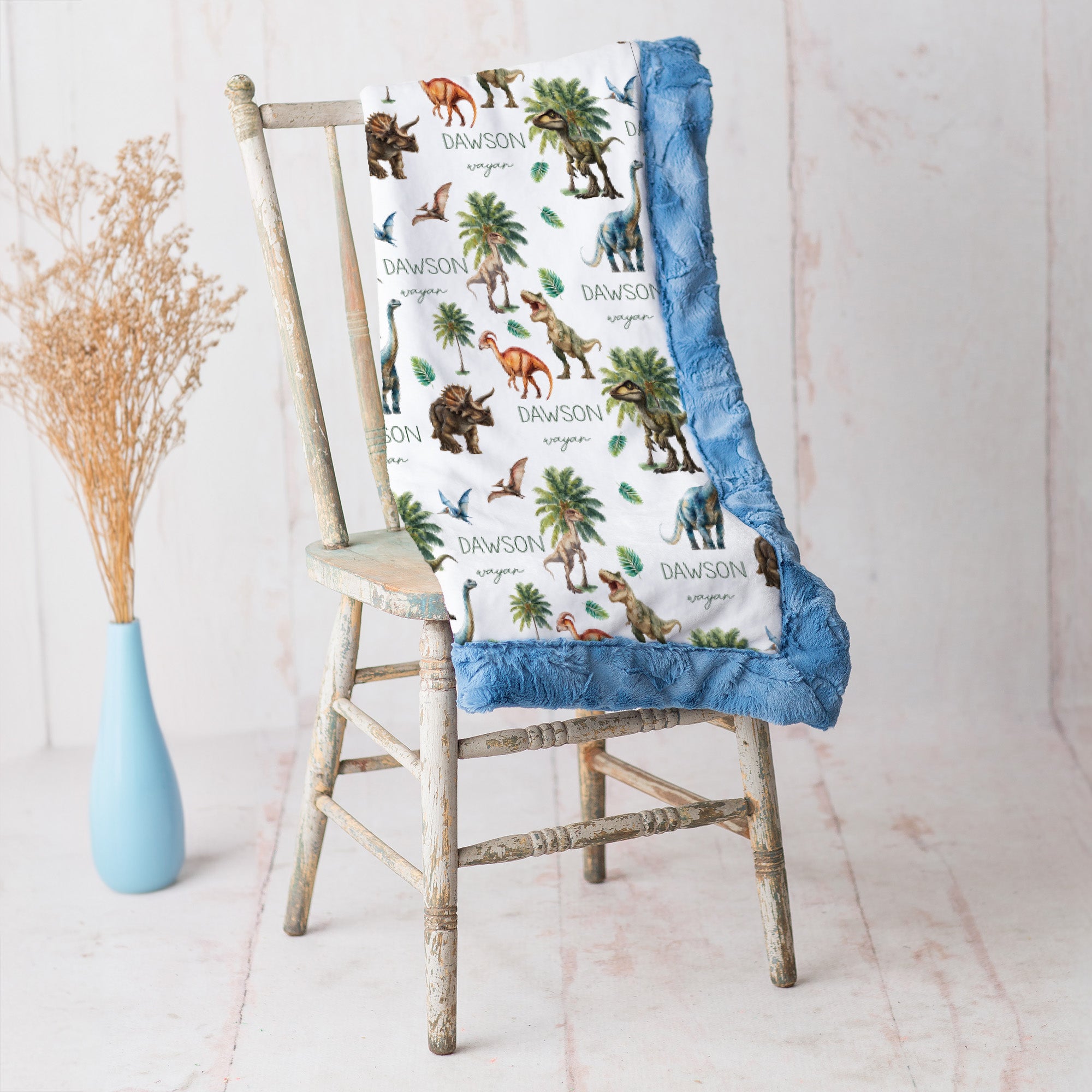 Close-up of personalized dinosaur minky blanket draped over vintage chair with blue trim