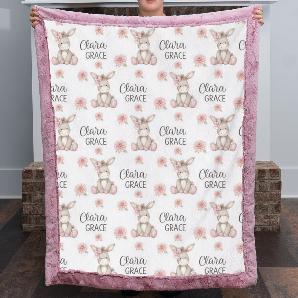 Personalized minky donkey baby blanket with mauve pink fur border held up by fireplace
