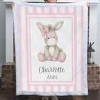 Personalized minky donkey baby blanket with pink stripe border held up by fireplace