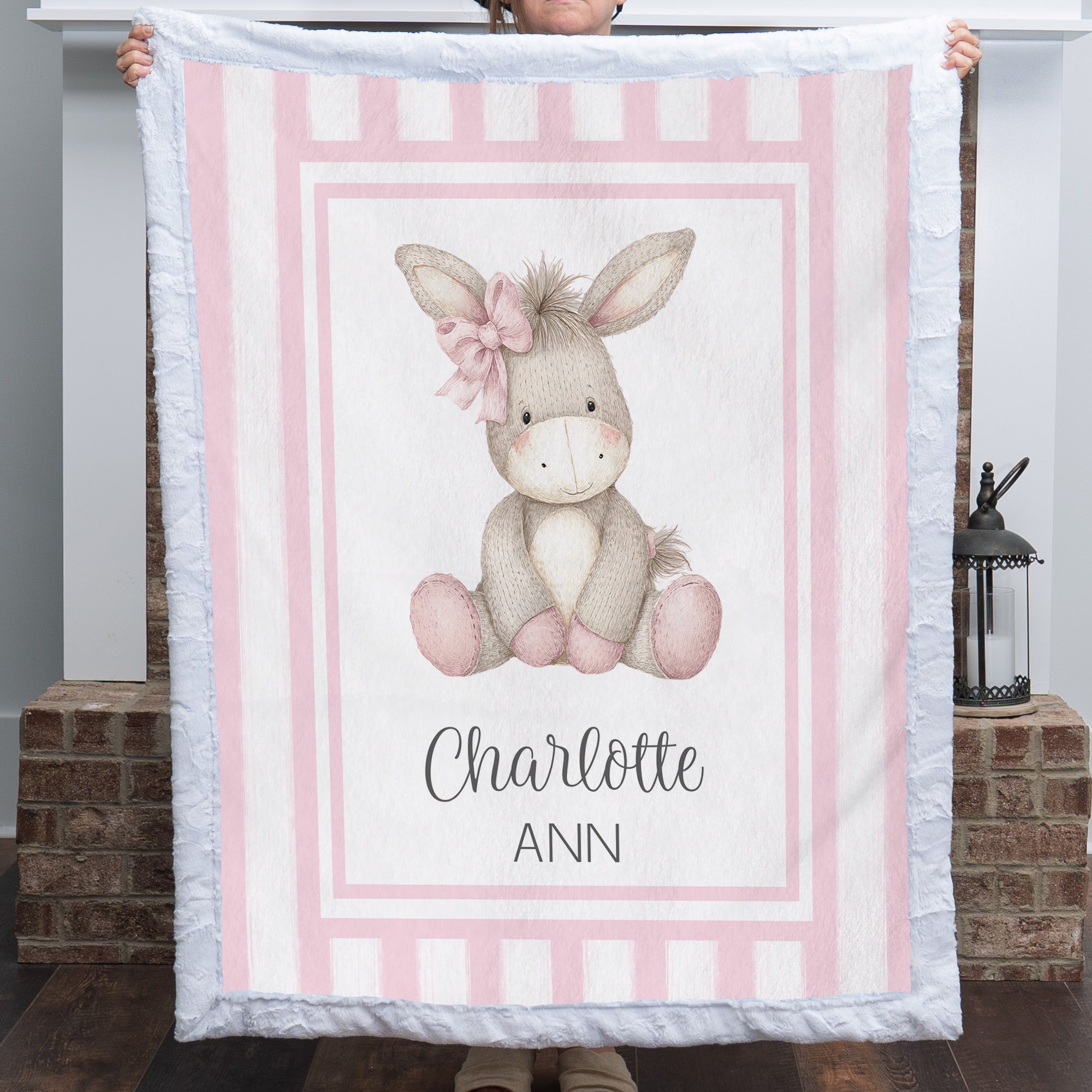 Personalized minky donkey baby blanket with pink stripe border held up by fireplace