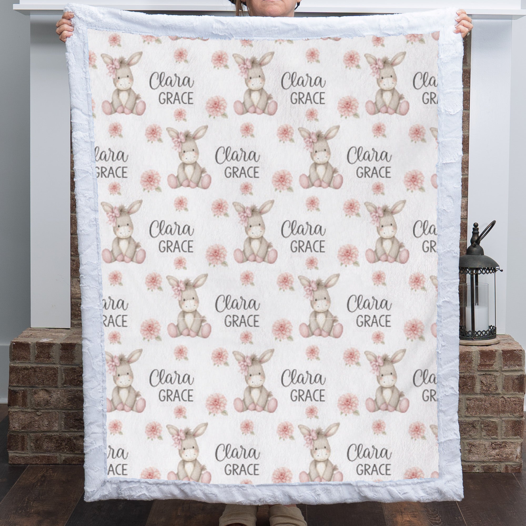Personalized minky donkey baby blanket with white fur border held up by fireplace