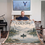Man holding up personalized fishing lake blanket in cozy living room by the fireplace