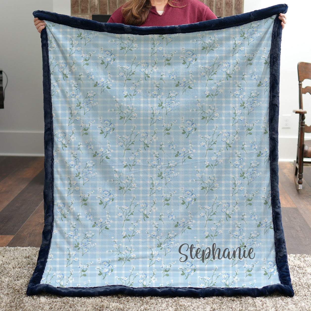 Personalized floral gingham Luxe Cuddle blanket with navy trim held up in living room