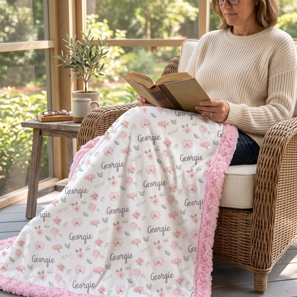 Woman reading on wicker porch chair with personalized floral minky blanket, pink rosette trim