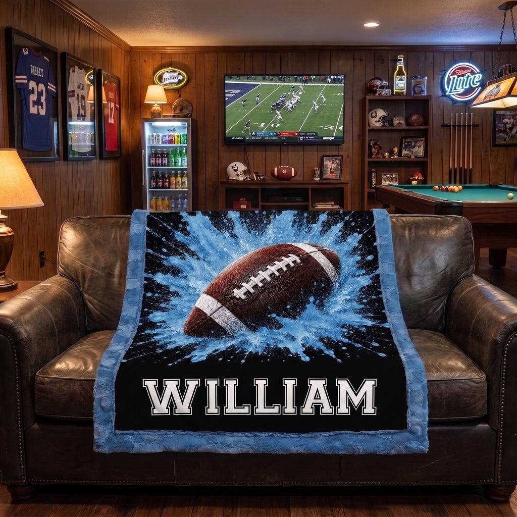 Personalized football minky baby blanket draped over leather chairs in a man cave with football on TV