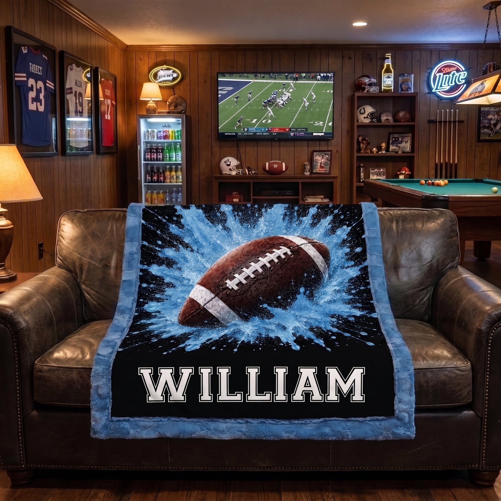 Personalized football minky baby blanket draped over leather chairs in a man cave with football on TV