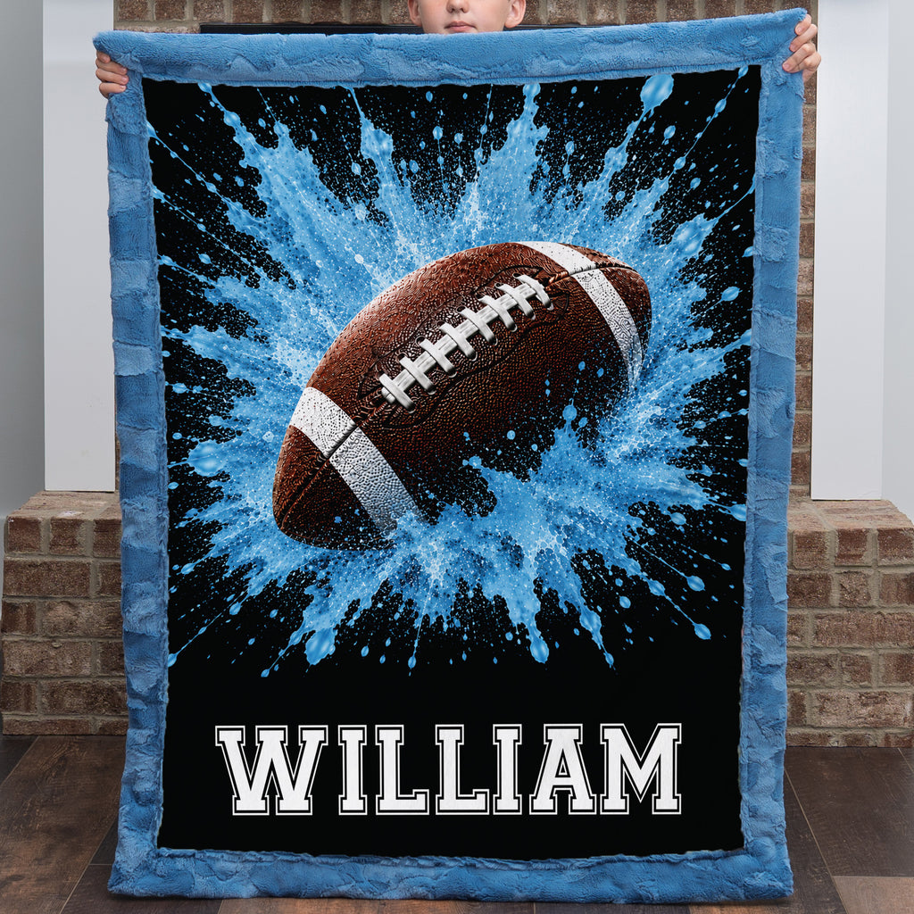 Personalized football minky baby blanket with name William, boy holding it against a brick wall