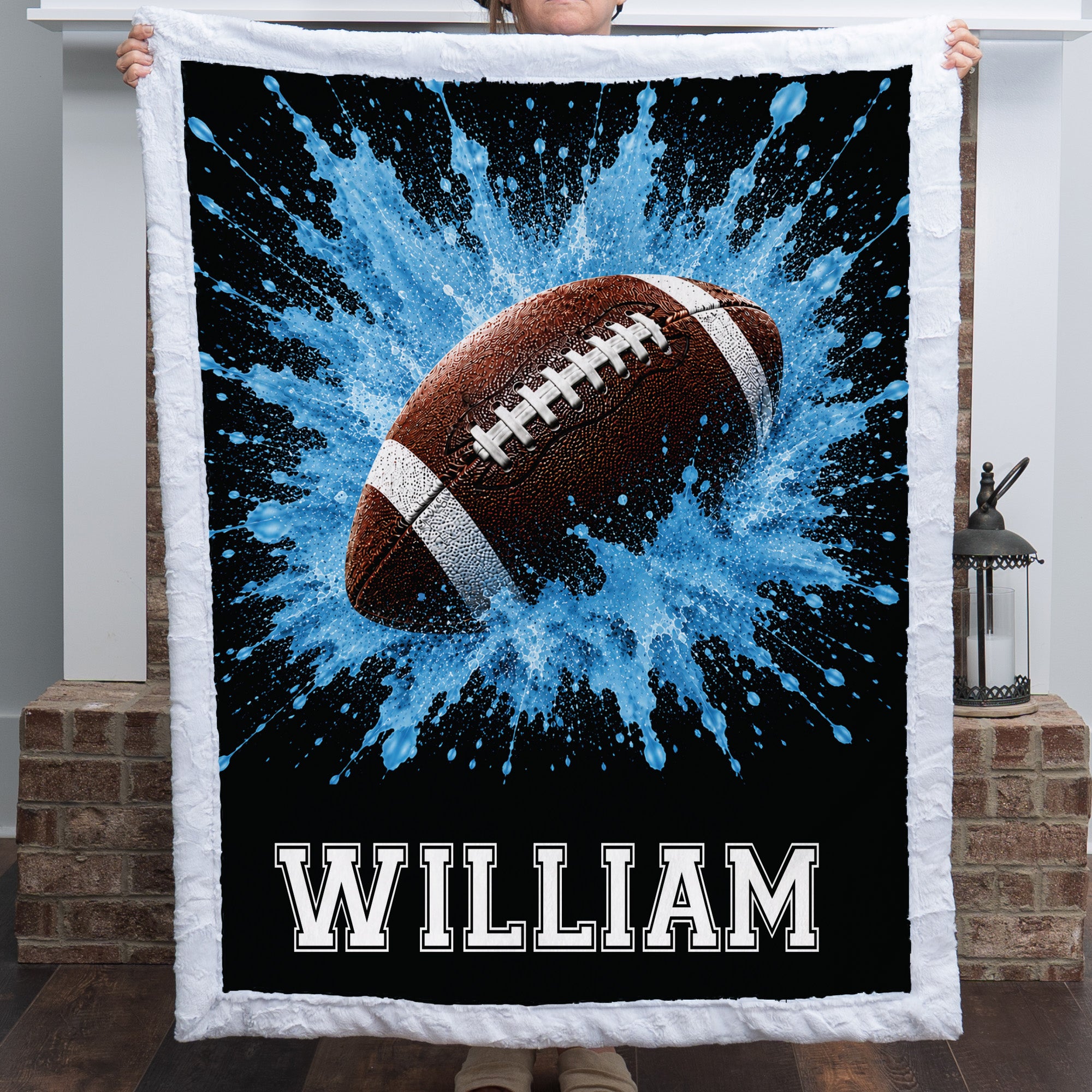 Personalized football minky baby blanket with white trim and name William, held near a fireplace