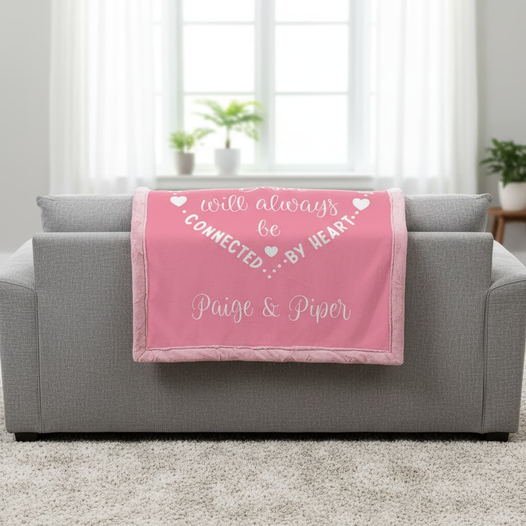 Pink blanket with text on a gray couch in a room with plants and windows.