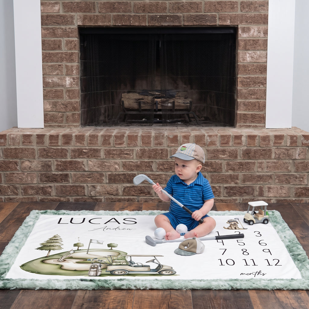 Baby boy sitting on personalized golf milestone blanket with toy clubs by fireplace
