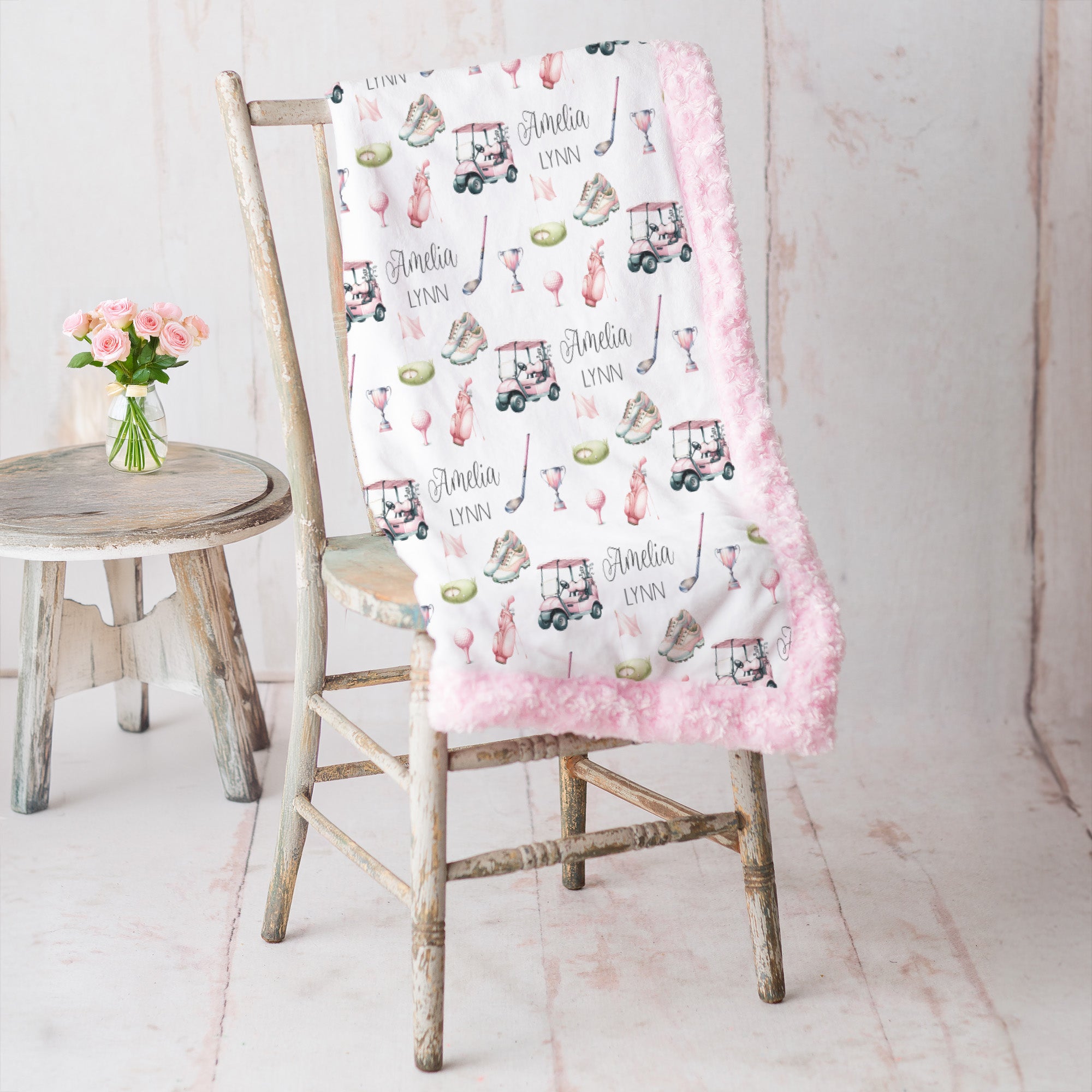 Personalized golf minky blanket with pink trim draped over vintage chair beside pink roses