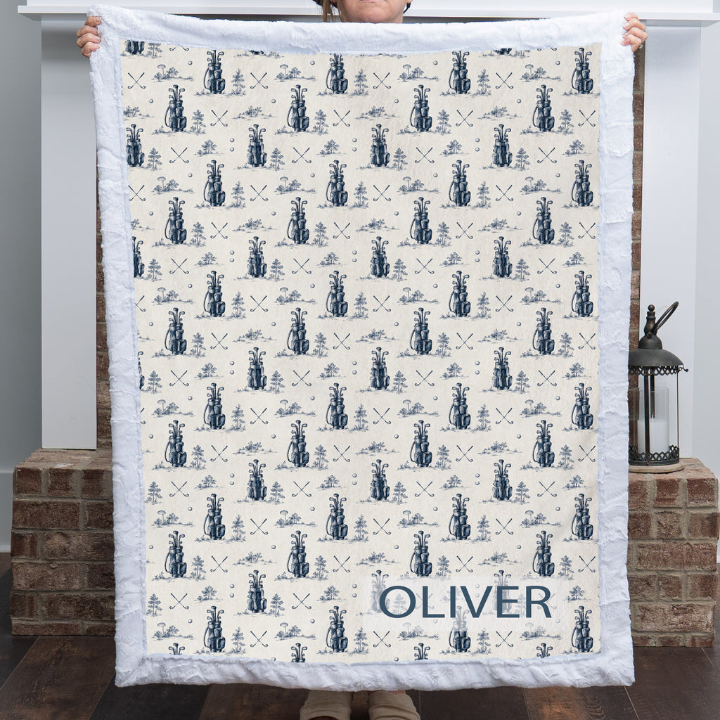Woman holding personalized golf-print minky blanket with name Oliver, white trim, by fireplace